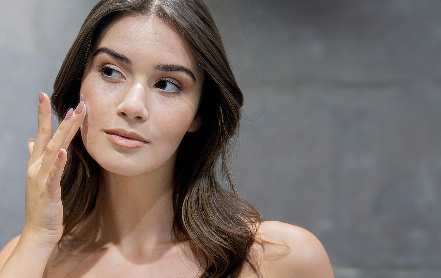 Woman applying skincare product to her face.